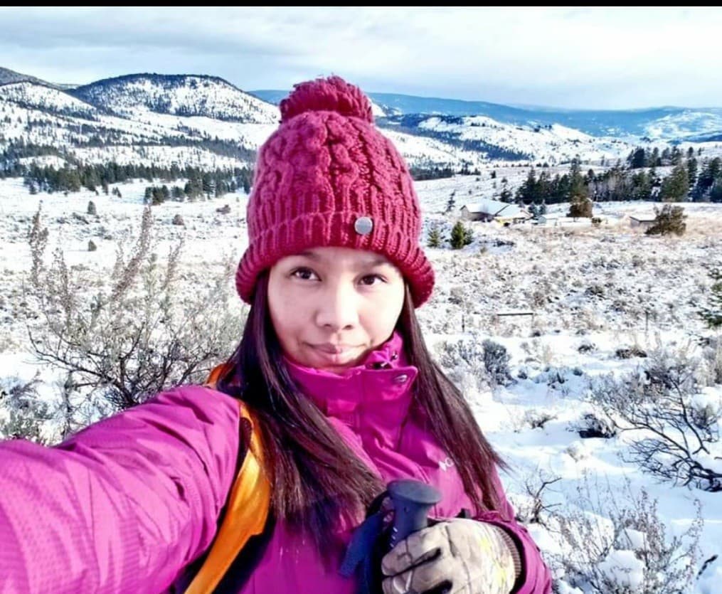 Woman in magenta winter gear taking a selfie while hiking in a snowy mountain landscape.